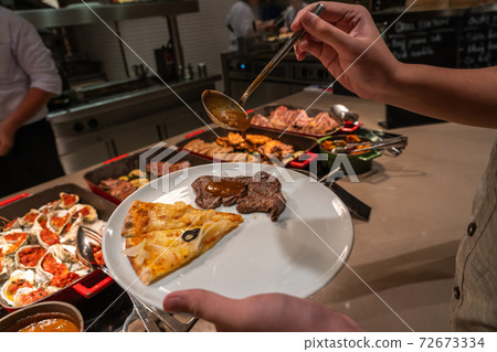 Human hand picking food into his plate in buffet restaurant 72673334