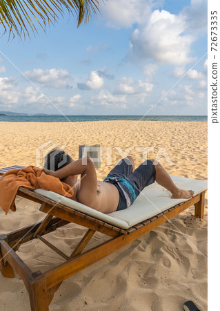 Vertical photo of Asian man sunbathing and reading book Vertical photo of Asian man sunbathing and reading book 72673335