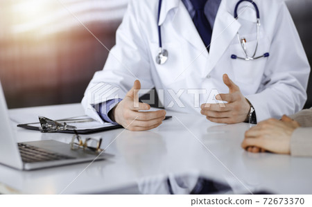 Unknown male doctor and patient woman discussing something while sittingin a darkened clinic, glare of light on the background. Close-up of hands Unknown male doctor and patient woman discussing something while sittingin a darkened clinic, glare of light on the background. Close-up of hands 72673370
