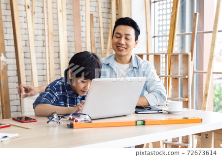 Asian father and son working together on laptop computer in carpentry workshop. Asian father and son working together on laptop computer in carpentry workshop. 72673614