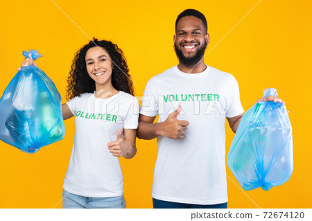 Couple Of Volunteers Holding Plastic Garbage Bags Over Yellow Background Couple Of Volunteers Holding Plastic Garbage Bags Over Yellow Background 72674120