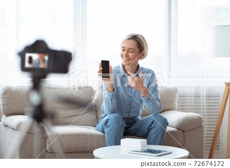 Happy young blogger making video review of new cellphone on professional camera, filming content for her vlog at home 72674172