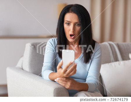 Surprised shocked mature woman using mobile phone Surprised shocked mature woman using mobile phone 72674179