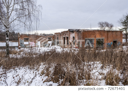 An old ruined brick building, dusted with snow on the river bank. 72675401