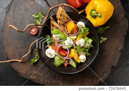 Vegetarian salad of vegetables, onions, cherry tomatoes, red and yellow bell peppers and greens with mozzarella cheese. Fresh summer salad appetizer. 72676645