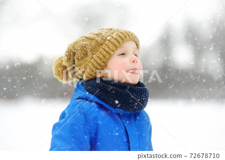 Funny little boy in blue winter clothes walks during a snowfall. Outdoors winter activities for kids Funny little boy in blue winter clothes walks during a snowfall. Outdoors winter activities for kids 72678710