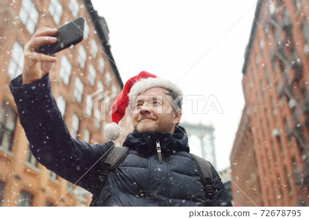 Middle aged man tourist in Santa Claus hat takes selfie on street near the Manhattan Bridge in NY Middle aged man tourist in Santa Claus hat takes selfie on street near the Manhattan Bridge in NY 72678795