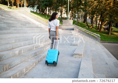 Woman poses with suitcase on the stairs in park 72679217