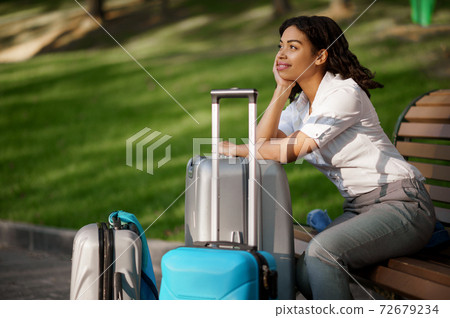 Woman with suitcase sitting on the bench in park 72679234