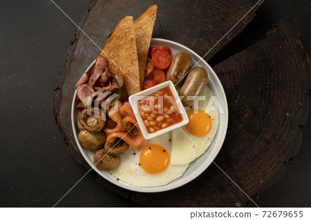 Fried eggs with beans in tomato sauce, fried mushrooms, bacon, salmon, chicken sausages, cherry tomatoes and toast. Hearty breakfast. 72679655