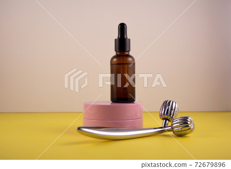 The concept of facial care and the fight against age-related changes. Metal roller, pink jar of cream and bottle of serum. Front veiw. The concept of facial care and the fight against age-related changes. Metal roller, pink jar of cream and bottle of serum. Front veiw. 72679896