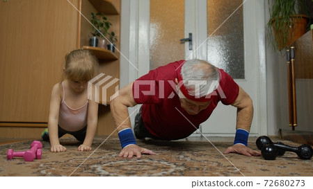 Child kid girl with senior grandfather in sportswear making sports workout push-up exercises at home Child kid girl with senior grandfather in sportswear making sports workout push-up exercises at home 72680273