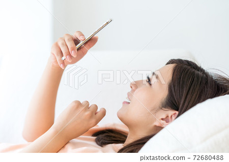 A young woman operating a smartphone in a room 72680488
