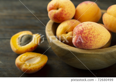 Fresh apricots in a wooden plate. Fruits are scattered on a wooden table. Fresh apricots in a wooden plate. Fruits are scattered on a wooden table. 72680499