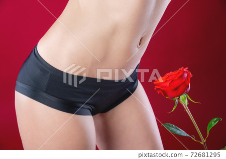 Close-up of a woman's belly and legs hair depilation in black underwear on a red background next to a red rose. The concept of hair removal and depilation on the abdomen in women Close-up of a woman's belly and legs hair depilation in black underwear on a red background next to a red rose. The concept of hair removal and depilation on the abdomen in women 72681295