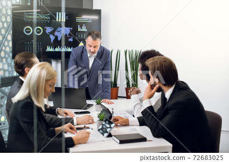 Mature male chief leans on the table and talking with his team, professional successful multiethnic male and female colleagues, working together over joint strategy of company Mature male chief leans on the table and talking with his team, professional successful multiethnic male and female colleagues, working together over joint strategy of company 72683025