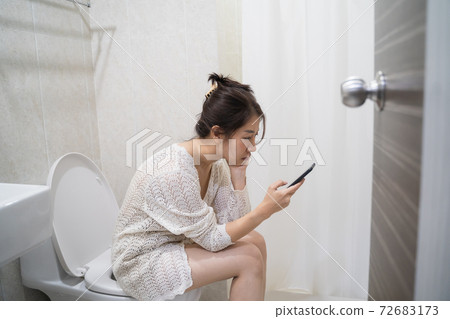 asian woman on toilet with cell phone. Woman sitting with mobile in toilet 72683173