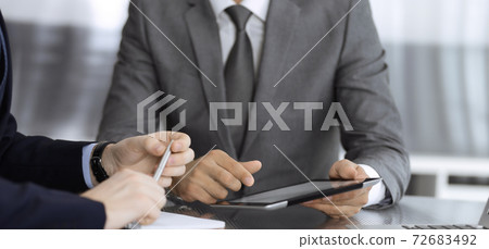 Unknown businessman using tablet computer and working together with his colleague while sits at the glass desk in modern office. Teamwork and partnership concept Unknown businessman using tablet computer and working together with his colleague while sits at the glass desk in modern office. Teamwork and partnership concept 72683492