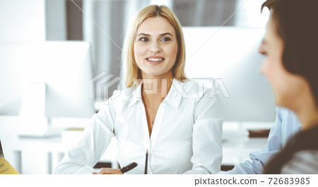 Group of business people discussing questions at meeting. Headshot of blonde businesswoman while smiling to her colleague at office negotiation. Teamwork and cooperation in corporate occupation 72683985