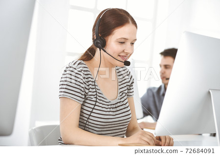 Casual dressed young woman using headset and computer while talking with customers online. Group of operators at work. Call center, business concept 72684091