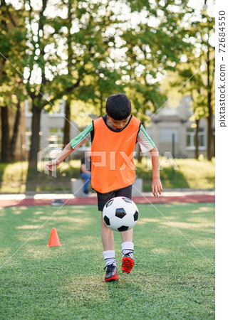 Motivated teen football player stuffs soccer ball on leg. Practicing sport exercises at artificial stadium. Motivated teen football player stuffs soccer ball on leg. Practicing sport exercises at artificial stadium. 72684550