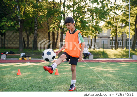 Motivated teen football player stuffs soccer ball on leg. Practicing sport exercises at artificial stadium. 72684551