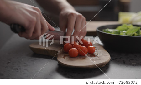 man hand cutting cherry tomatoes into halves on wood board on home kitchen 72685072