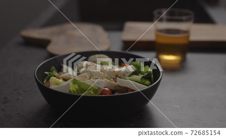 salad with mozzarella and tomatoes in black bowl and apple cider in glass on concrete countertop 72685154