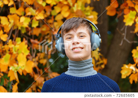 portrait of a teenager listening to music by headphones, relaxing in autumn city park, bright yellow maple leaves as background portrait of a teenager listening to music by headphones, relaxing in autumn city park, bright yellow maple leaves as background 72685605