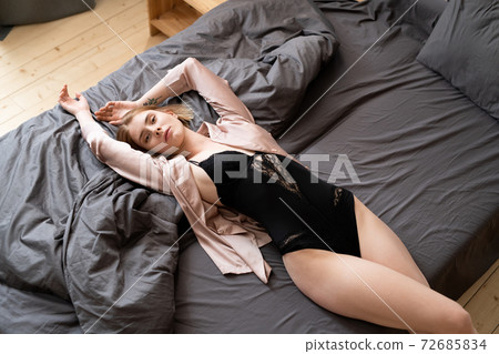 Young relaxed female in black lingerie keeping arms stretched while lying on bed 72685834