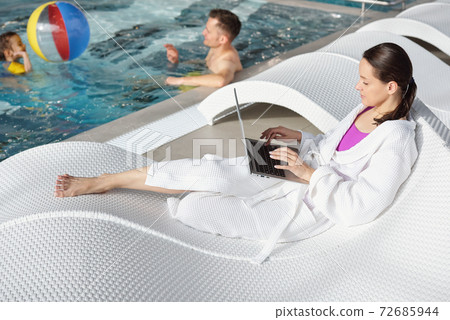Young man and cute little girl playing in swimming pool while woman using laptop Young man and cute little girl playing in swimming pool while woman using laptop 72685944