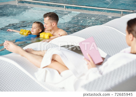 Young man supporting his little daughter in safety sleeves during swimming 72685945