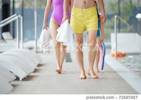 Legs of young couple and their little daughter in swimwear moving forwards 72685987