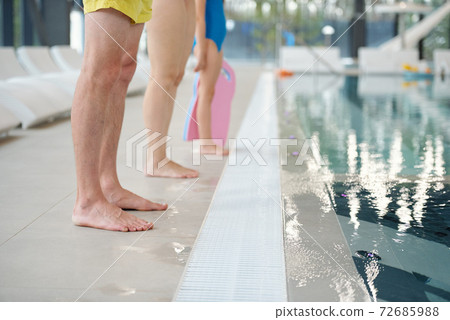 Legs of father, mother and little daughter in swimwear standing by poolside Legs of father, mother and little daughter in swimwear standing by poolside 72685988