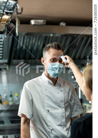 Male chef looking at woman with thermometer measuring his body temperature Male chef looking at woman with thermometer measuring his body temperature 72686009