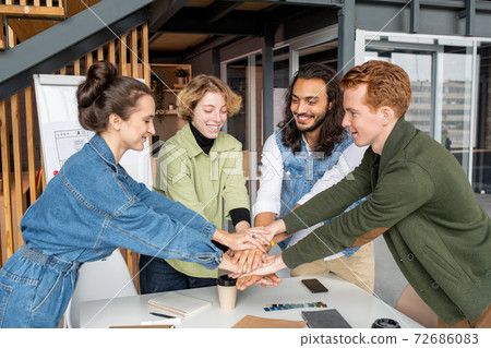 Happy young intercultural designers or software developers making pile of hands 72686083