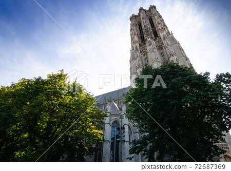 Mechelen, Belgium, August 2019. The imposing cathedral features a 97-meter bell tower in Gothic style. Beautiful summer day with blue sky. Mechelen, Belgium, August 2019. The imposing cathedral features a 97-meter bell tower in Gothic style. Beautiful summer day with blue sky. 72687369