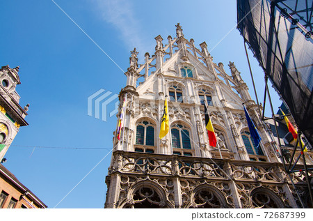 Mechelen, Belgium, August 2019. The town hall overlooks the large square, the Grote Markt. It stands out for the elegance of the facade and the flags. In the square they are setting up a stage 72687399