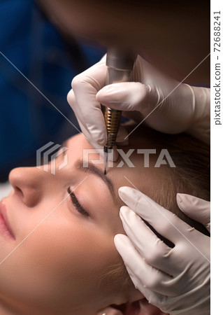 Permanent eyebrow makeup. Cosmetologist applying tattooing of eyebrows. 72688241