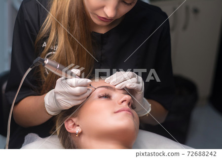 Permanent eyebrow makeup. Cosmetologist applying tattooing of eyebrows. 72688242