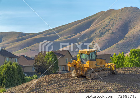 Yellow bulldozer on a construction site overlooking homes mountain and sky 72689783