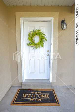 Close up of a home entrance with white front door decorated with green wreath 72689832