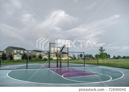 Basketball courts at a park near multi storey family homes under cloudy sky 72690048