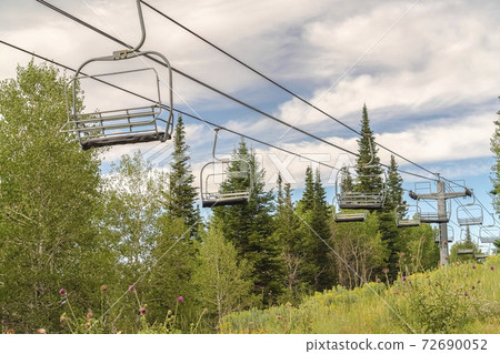 Chairlifts on cables with view of ski resort covered in greenery during summer Chairlifts on cables with view of ski resort covered in greenery during summer 72690052