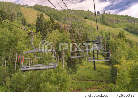Vibrant green summer landscape of trees and mountain beneath chairlifts 72690088