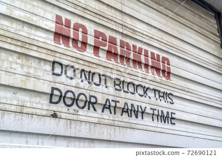 Close up of No Parking sign painted on the corrugated metal door of a building 72690121