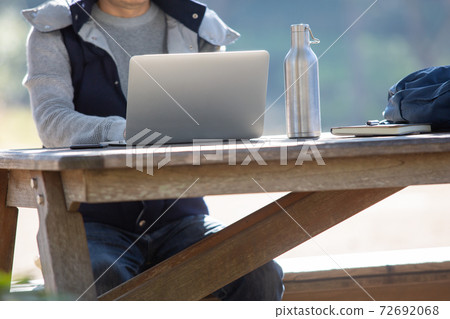 A man heading to a computer on an outdoor bench A man heading to a computer on an outdoor bench 72692068