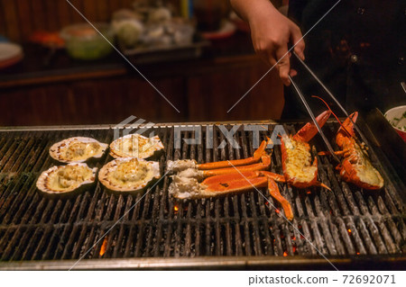 Close up of hand grilling seafood on barbecue pan Close up of hand grilling seafood on barbecue pan 72692071