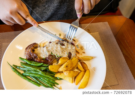 Hands using knife and fork cutting beefsteak on plate Hands using knife and fork cutting beefsteak on plate 72692078