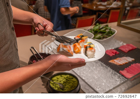 Man using tongs picking assortment of sushi in buffet meal 72692647